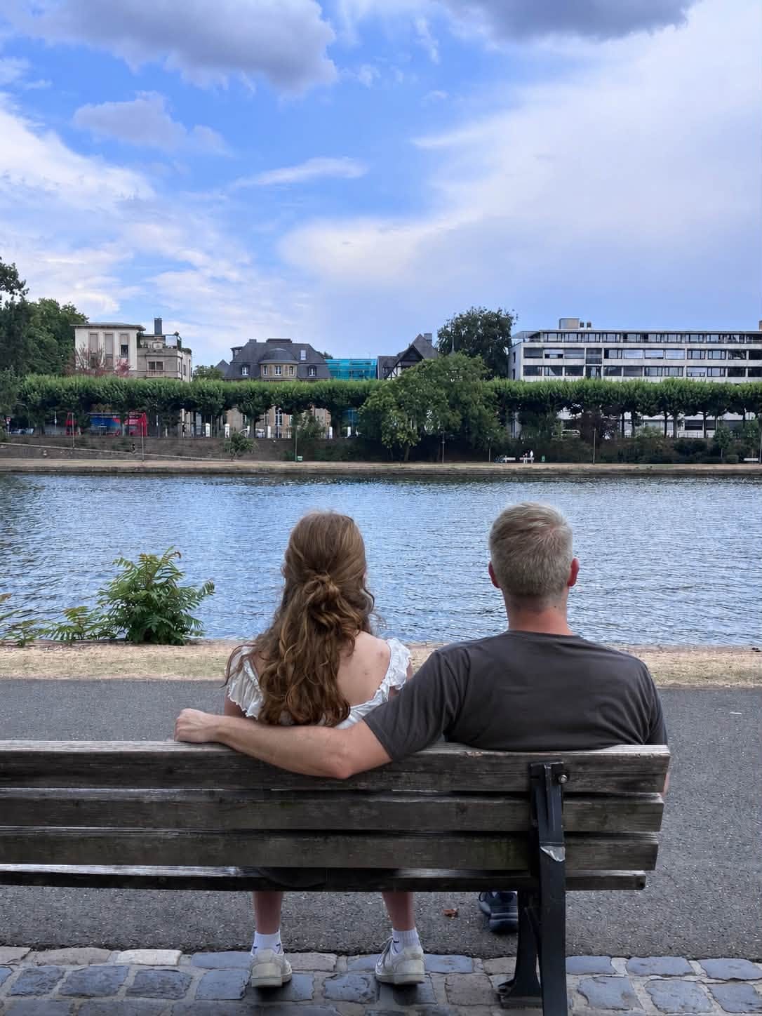 Dave with his arm around one of the girls on a bench, backs to the camera, looking across the Main river